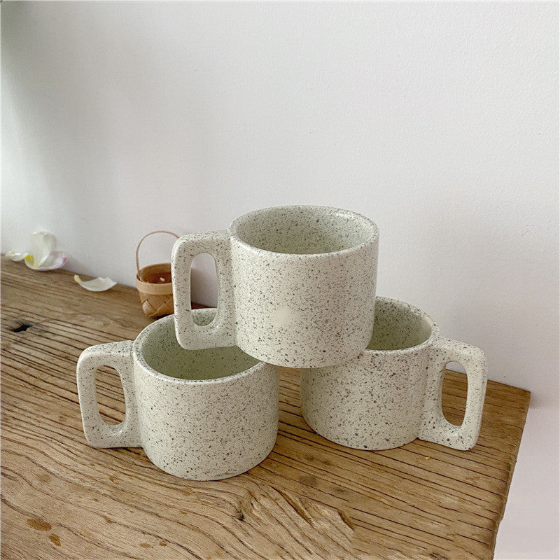 Three ceramic mugs with speckled texture on a wooden surface.