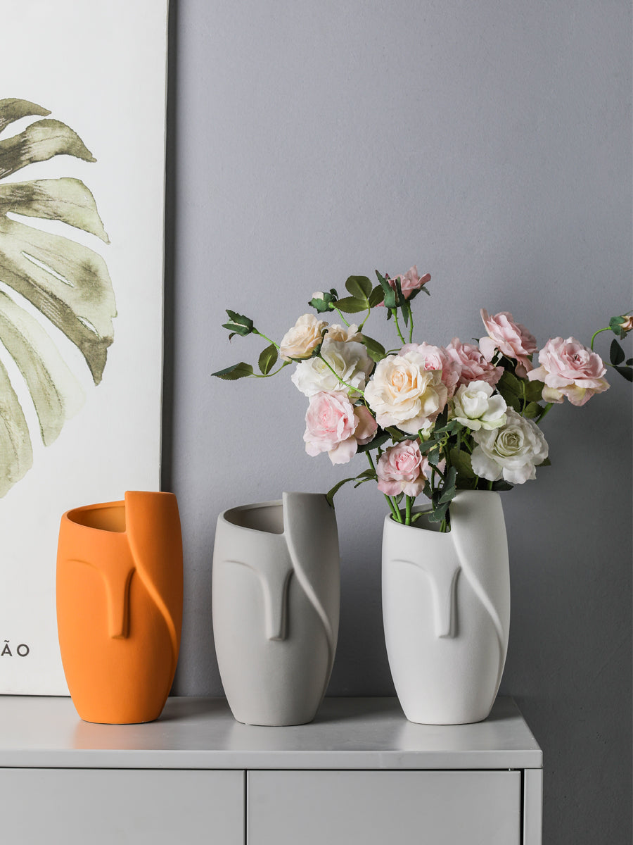 Three vases on a shelf with a bouquet of flowers in the center against a gray wall.