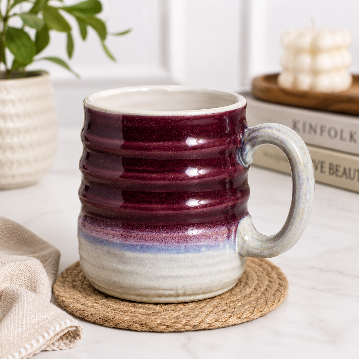A ceramic mug with a deep burgundy and purple glaze fading into a light gray and white base, sitting on a woven coaster on a white marble surface.