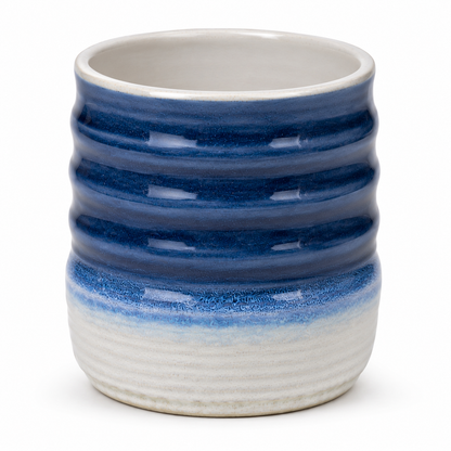 A small ceramic cup with a ribbed, wavy design, featuring a glossy dark blue to white gradient glaze on a white background.