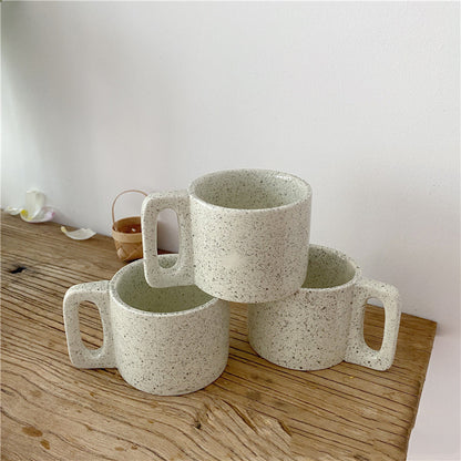 Three ceramic mugs with speckled texture on a wooden surface.