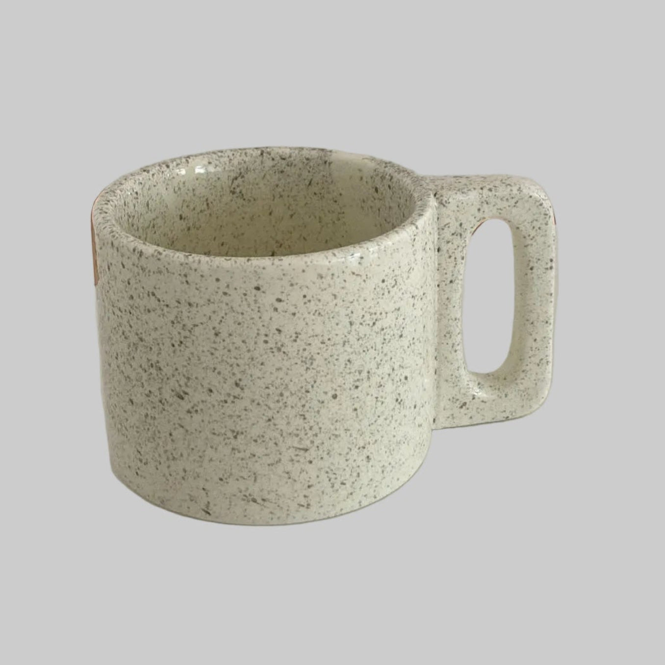 Speckled green mug on a white surface with a neutral background