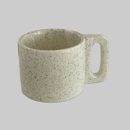 Speckled green mug on a white surface with a neutral background