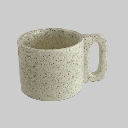Speckled green mug on a white surface with a neutral background
