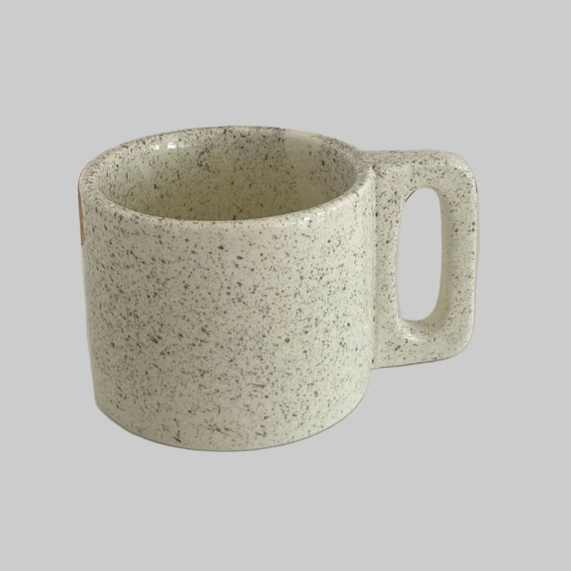 Speckled green mug on a white surface with a neutral background