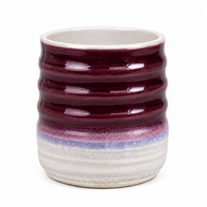 A handmade ceramic cup with a ribbed texture, featuring a deep burgundy glazed upper half and a textured off-white lower half with a subtle purple band.