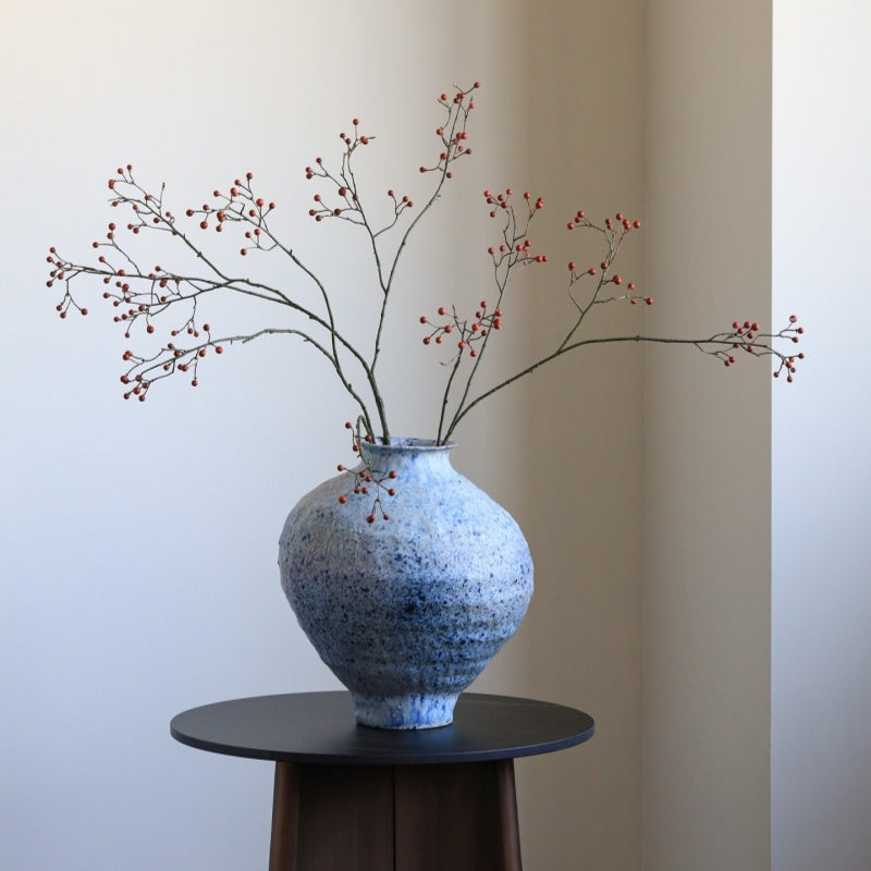 Blue textured vase with branches on a black pedestal against a beige wall