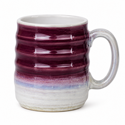 A handmade ceramic mug with a wavy ribbed design, featuring a deep burgundy glazed upper section, a light blue band, and a natural off-white unglazed base and handle.
