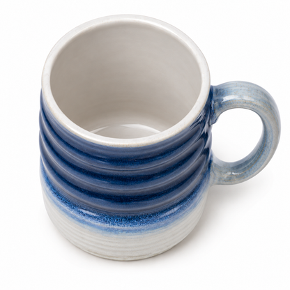 A ceramic mug with a ribbed exterior featuring a blue and gray gradient glaze, and a smooth off-white interior, shown on a white background.