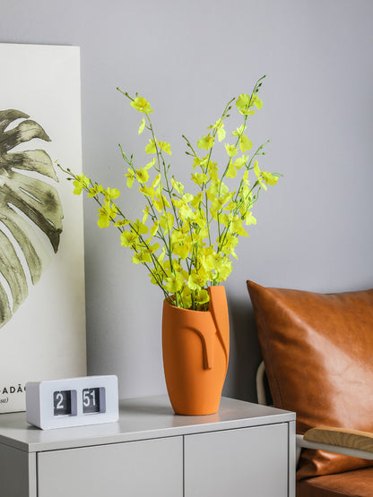 Vase with yellow flowers on a table next to a calendar and a brown pillow.