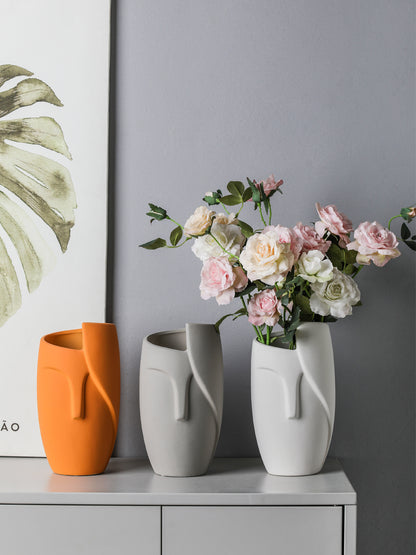 Three vases on a shelf with a bouquet of flowers in the center against a gray wall.