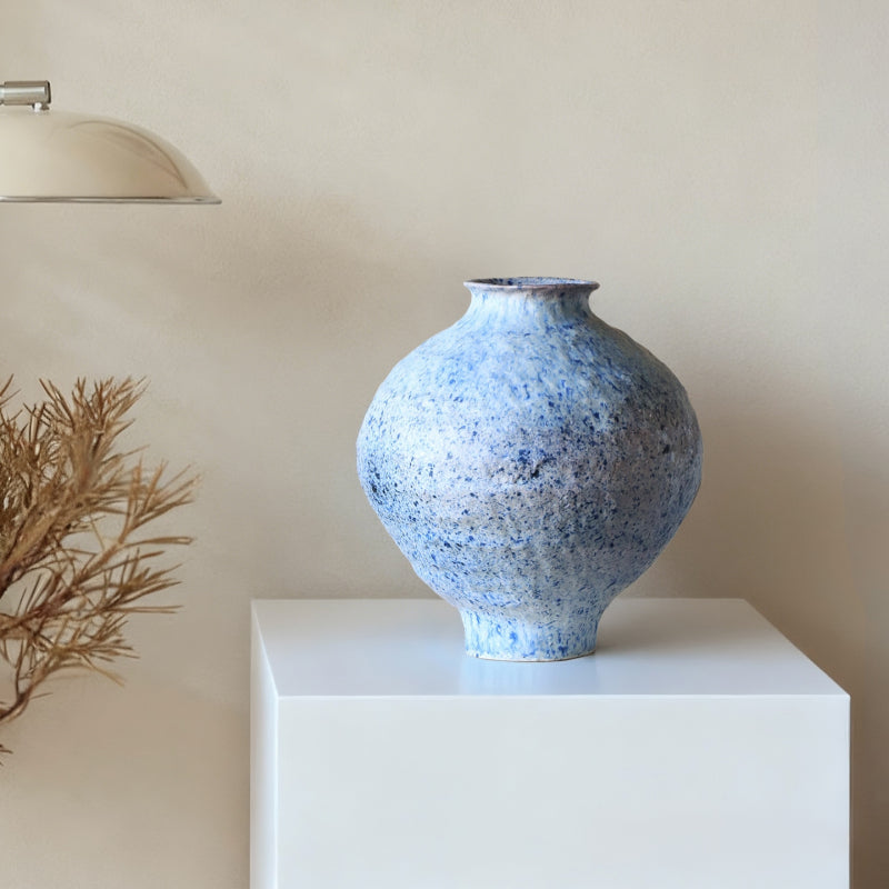 Blue speckled vase on a white pedestal against a beige wall