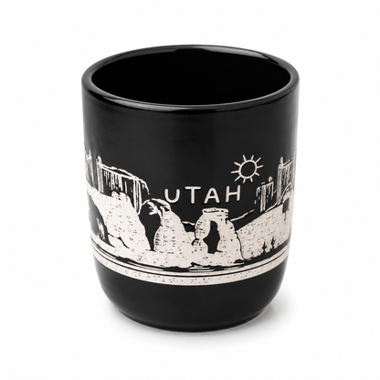 A black ceramic travel tumbler featuring a white distressed graphic of Arches National Park in Utah, with the word 'UTAH' and a sun icon printed on the side.