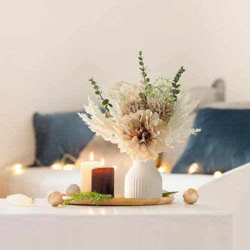 Decorative arrangement with flowers and candles on a table in a softly lit room.
